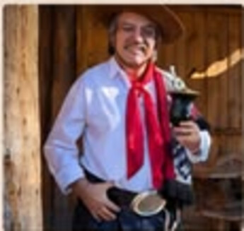 Jorge Guedes em pé com cuia de chimarrão, chapéu e lenço vermelho