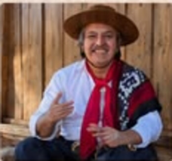 Jorge Guedes sentado, sorrindo, com poncho sobre o ombro